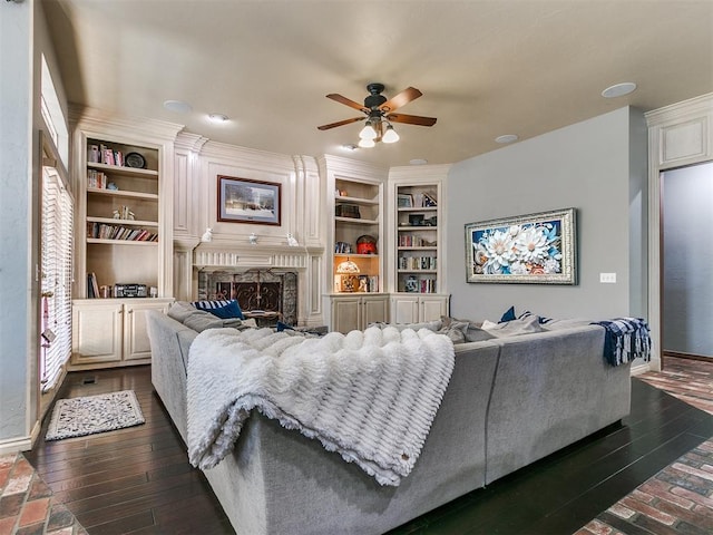 living room with a premium fireplace, ceiling fan, built in features, and dark wood-type flooring