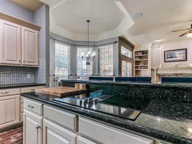 kitchen with backsplash, dark stone counters, ceiling fan with notable chandelier, hanging light fixtures, and black electric cooktop