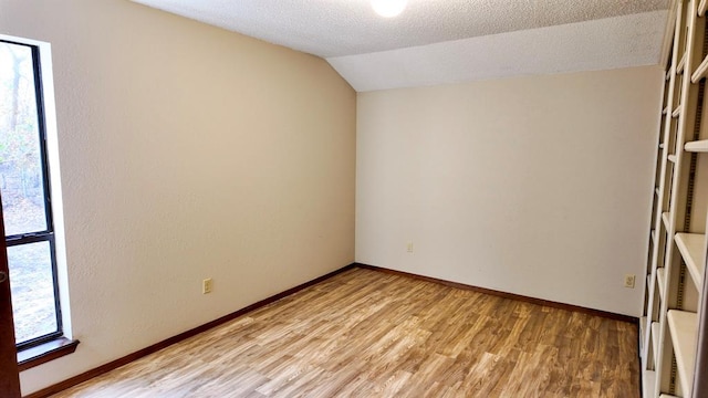 spare room with light hardwood / wood-style floors, vaulted ceiling, and a textured ceiling