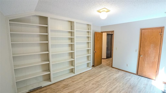 unfurnished bedroom featuring lofted ceiling, light hardwood / wood-style floors, and a textured ceiling