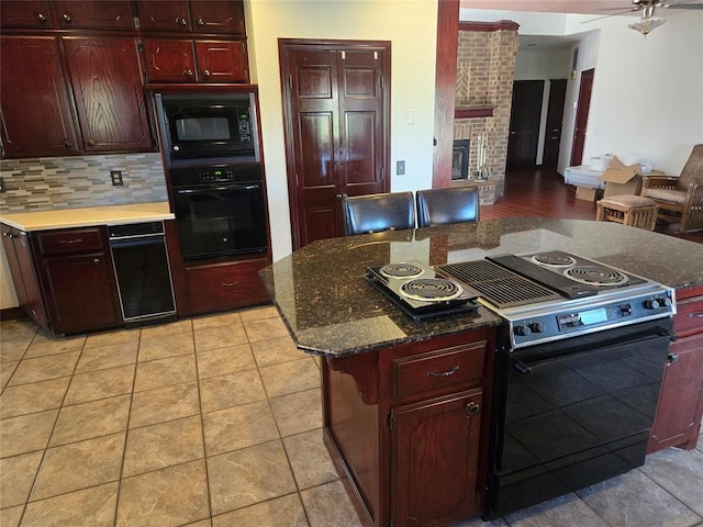 kitchen featuring black appliances, a brick fireplace, decorative backsplash, light tile patterned floors, and a kitchen island