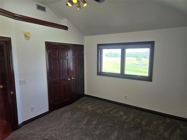 unfurnished bedroom with a closet, lofted ceiling, and dark colored carpet