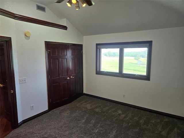 unfurnished bedroom with dark colored carpet, a closet, lofted ceiling, and ceiling fan