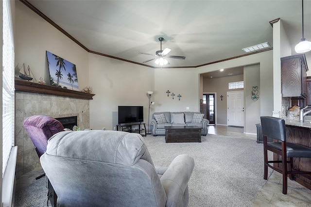 living room featuring a tile fireplace, light colored carpet, ceiling fan, and crown molding