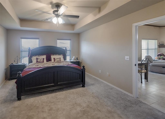 carpeted bedroom with a raised ceiling, multiple windows, and ceiling fan