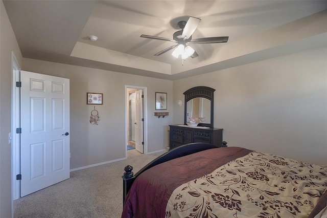 carpeted bedroom with a raised ceiling, connected bathroom, and ceiling fan