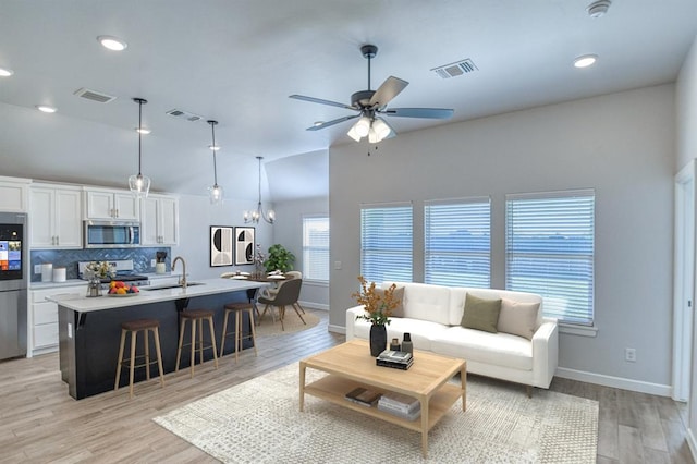 living room with ceiling fan with notable chandelier, light hardwood / wood-style floors, and sink