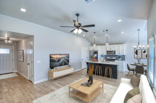 living room featuring ceiling fan with notable chandelier, light hardwood / wood-style flooring, vaulted ceiling, and sink