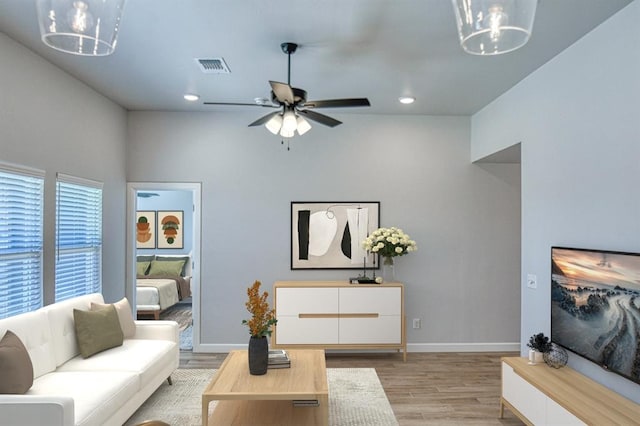 living room featuring ceiling fan with notable chandelier and light wood-type flooring