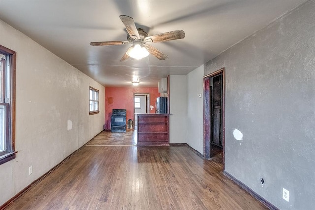 unfurnished room with hardwood / wood-style flooring, a wood stove, and ceiling fan