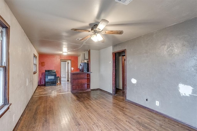 interior space featuring wood-type flooring, ceiling fan, and a wood stove