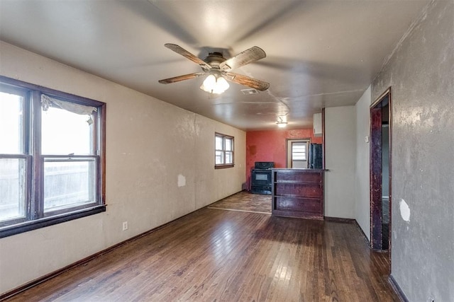 unfurnished living room with ceiling fan, wood-type flooring, visible vents, and a wood stove