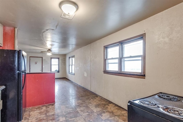 kitchen with a textured wall, a ceiling fan, freestanding refrigerator, and electric range oven