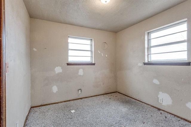 carpeted empty room with plenty of natural light, a textured ceiling, and baseboards