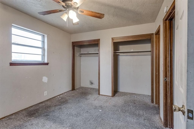 unfurnished bedroom with a textured ceiling, two closets, a ceiling fan, and carpet floors