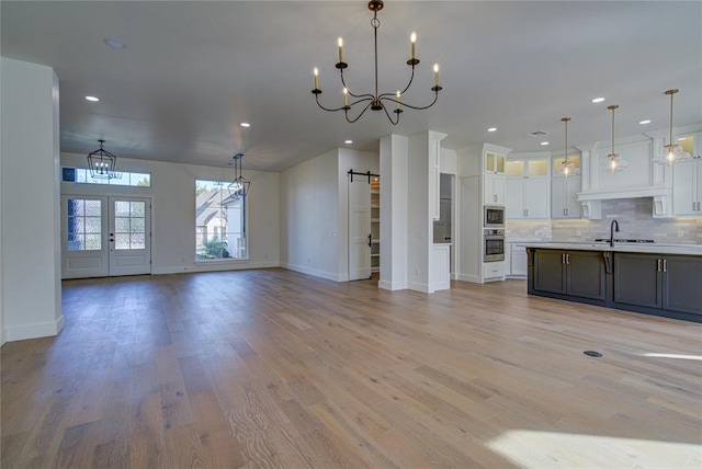 kitchen with a barn door, backsplash, pendant lighting, white cabinets, and light wood-type flooring