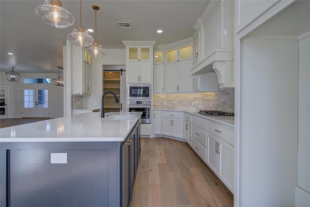 kitchen featuring sink, pendant lighting, a kitchen island with sink, white cabinets, and light wood-type flooring