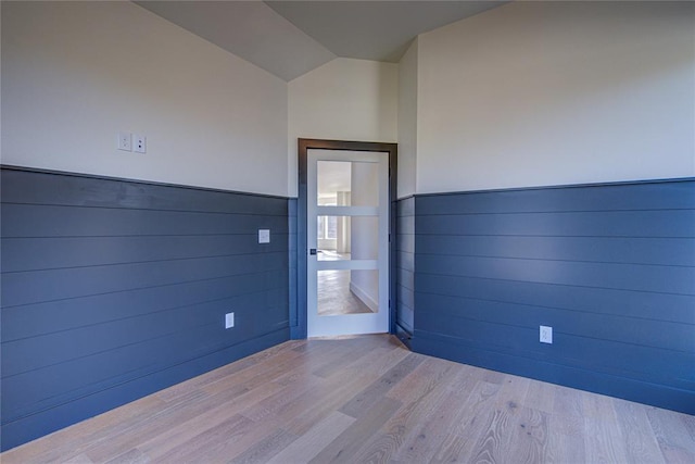 unfurnished room featuring wood walls, lofted ceiling, and light hardwood / wood-style flooring