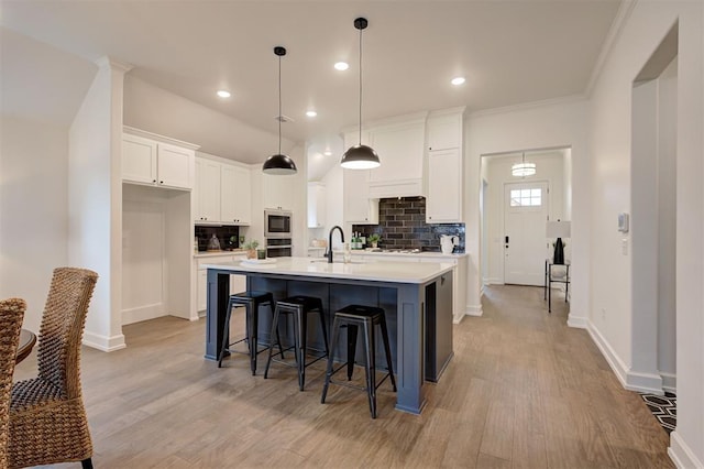 kitchen with pendant lighting, tasteful backsplash, sink, white cabinets, and a center island with sink