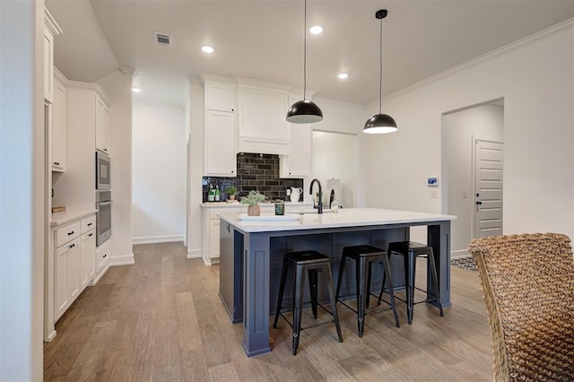 kitchen with tasteful backsplash, decorative light fixtures, a center island with sink, and white cabinets