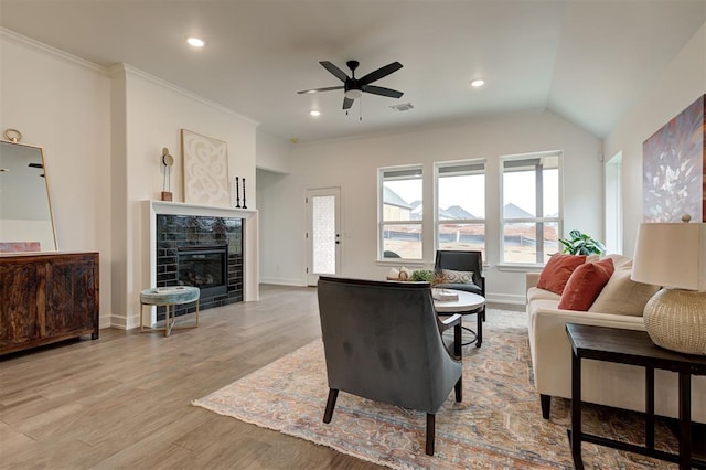 living room with lofted ceiling, crown molding, light hardwood / wood-style flooring, a tile fireplace, and ceiling fan