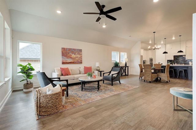 living room featuring lofted ceiling, ceiling fan with notable chandelier, and light wood-type flooring