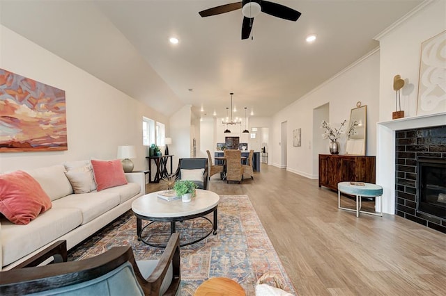 living room featuring crown molding, ceiling fan with notable chandelier, a tile fireplace, and light wood-type flooring