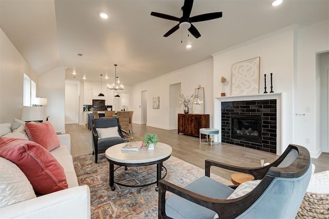 living room featuring wood-type flooring, vaulted ceiling, ornamental molding, a tile fireplace, and ceiling fan with notable chandelier