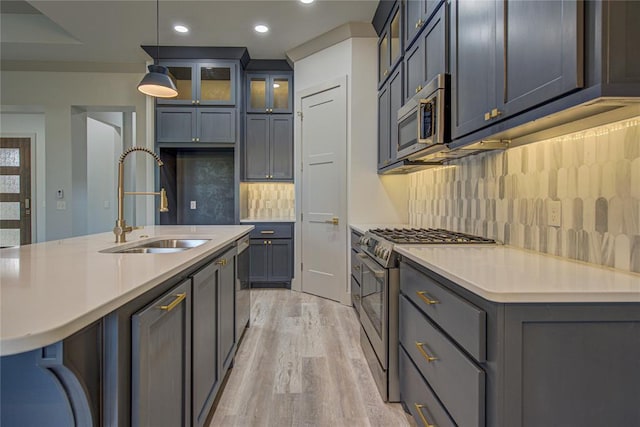 kitchen featuring appliances with stainless steel finishes, light wood-type flooring, sink, decorative light fixtures, and an island with sink