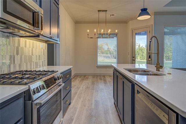 kitchen featuring sink, ornamental molding, appliances with stainless steel finishes, decorative light fixtures, and light hardwood / wood-style floors