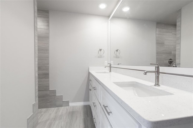 bathroom featuring a sink, baseboards, double vanity, and recessed lighting