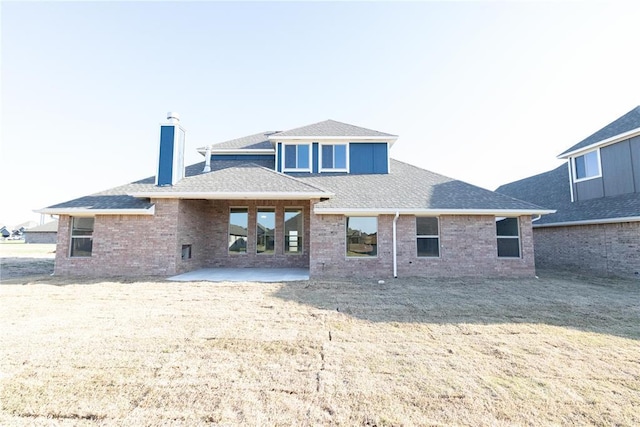 back of house featuring a patio, a chimney, a shingled roof, and brick siding