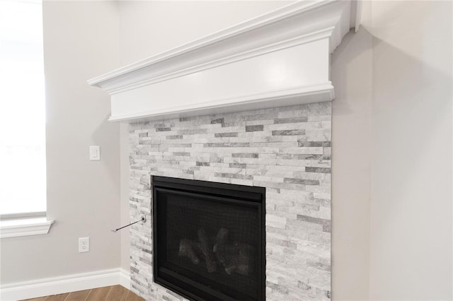 details featuring a stone fireplace, wood finished floors, and baseboards