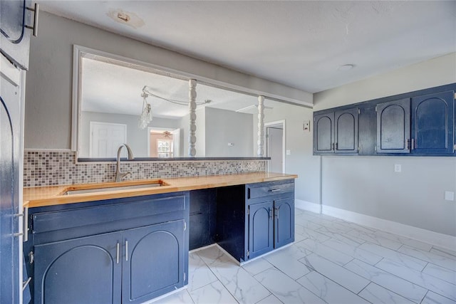 kitchen featuring backsplash, butcher block counters, blue cabinetry, and sink