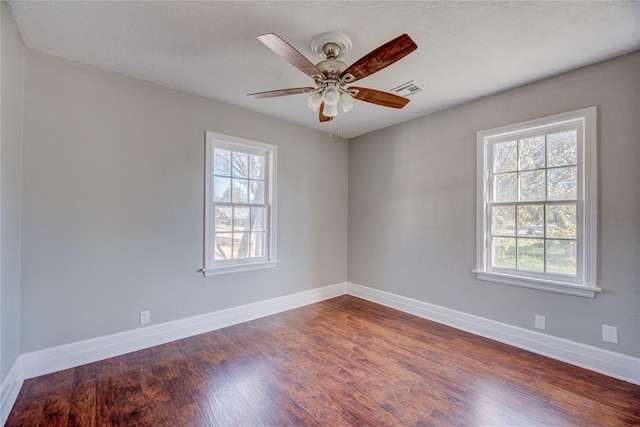 spare room featuring a wealth of natural light, ceiling fan, and dark wood-type flooring