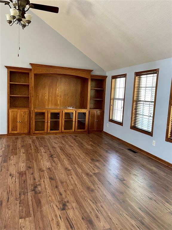 unfurnished living room with a textured ceiling, ceiling fan, dark wood-type flooring, and vaulted ceiling