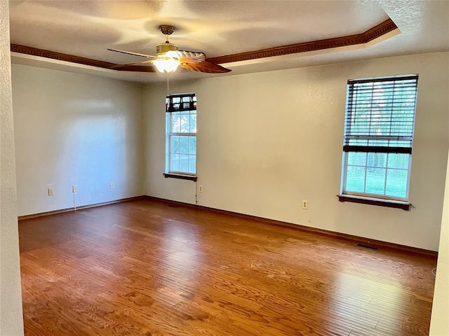 empty room with a tray ceiling, a wealth of natural light, hardwood / wood-style floors, and ceiling fan