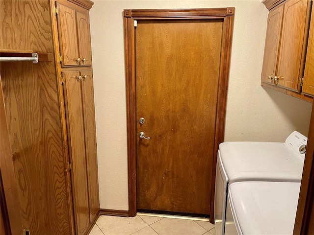 clothes washing area featuring light tile patterned floors, washing machine and dryer, and cabinets