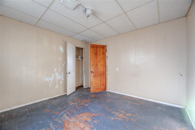 unfurnished room with a drop ceiling and wood walls