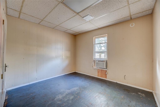 empty room with a paneled ceiling, wooden walls, and cooling unit