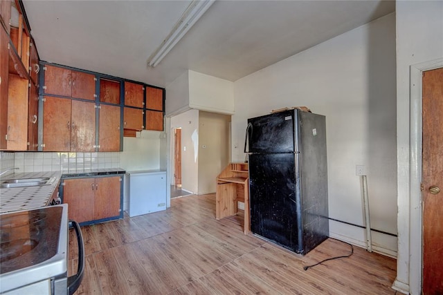 kitchen featuring sink, black fridge, light hardwood / wood-style flooring, backsplash, and stove