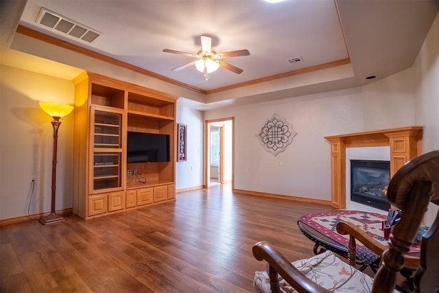 living room featuring hardwood / wood-style flooring, a raised ceiling, ceiling fan, and ornamental molding