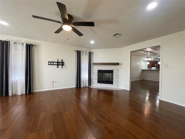 unfurnished living room featuring a fireplace, ceiling fan, dark hardwood / wood-style flooring, and a textured ceiling