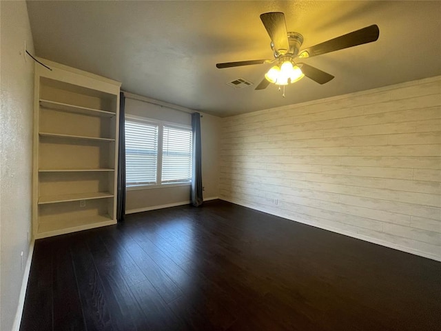 empty room with ceiling fan, wood walls, and dark wood-type flooring