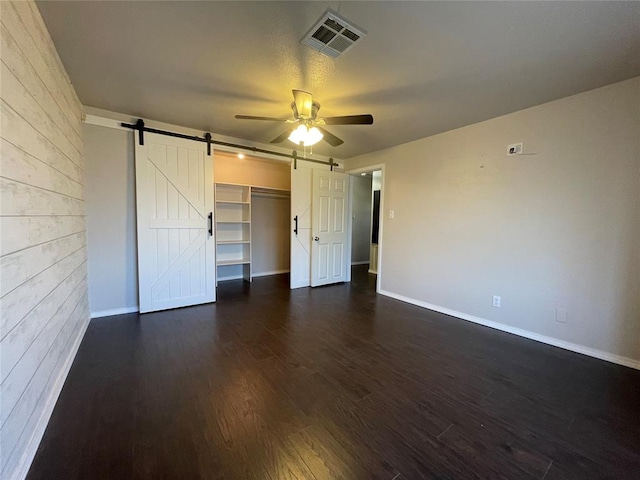 unfurnished bedroom featuring dark hardwood / wood-style flooring, ceiling fan, a barn door, a spacious closet, and a closet