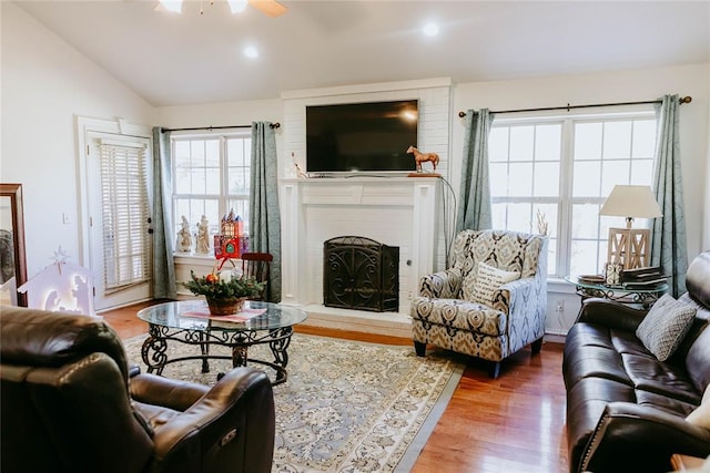 living room featuring hardwood / wood-style floors, vaulted ceiling, a brick fireplace, and ceiling fan