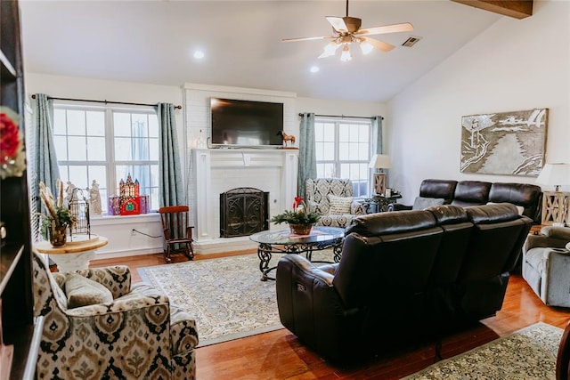 living room with hardwood / wood-style flooring, vaulted ceiling with beams, ceiling fan, and a fireplace