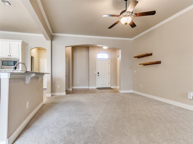 unfurnished living room featuring ceiling fan, light colored carpet, and ornamental molding