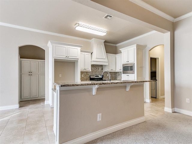 kitchen with stainless steel appliances, a breakfast bar area, a center island with sink, white cabinets, and custom range hood