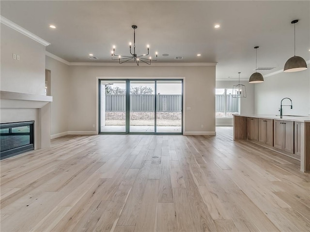 unfurnished living room with crown molding, light hardwood / wood-style flooring, an inviting chandelier, and sink